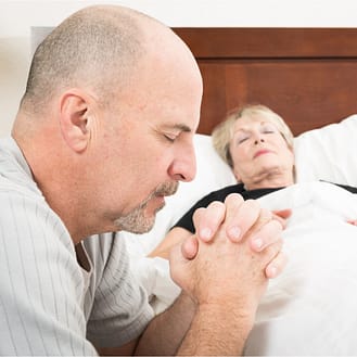 Man praying for a sick lady by her bed